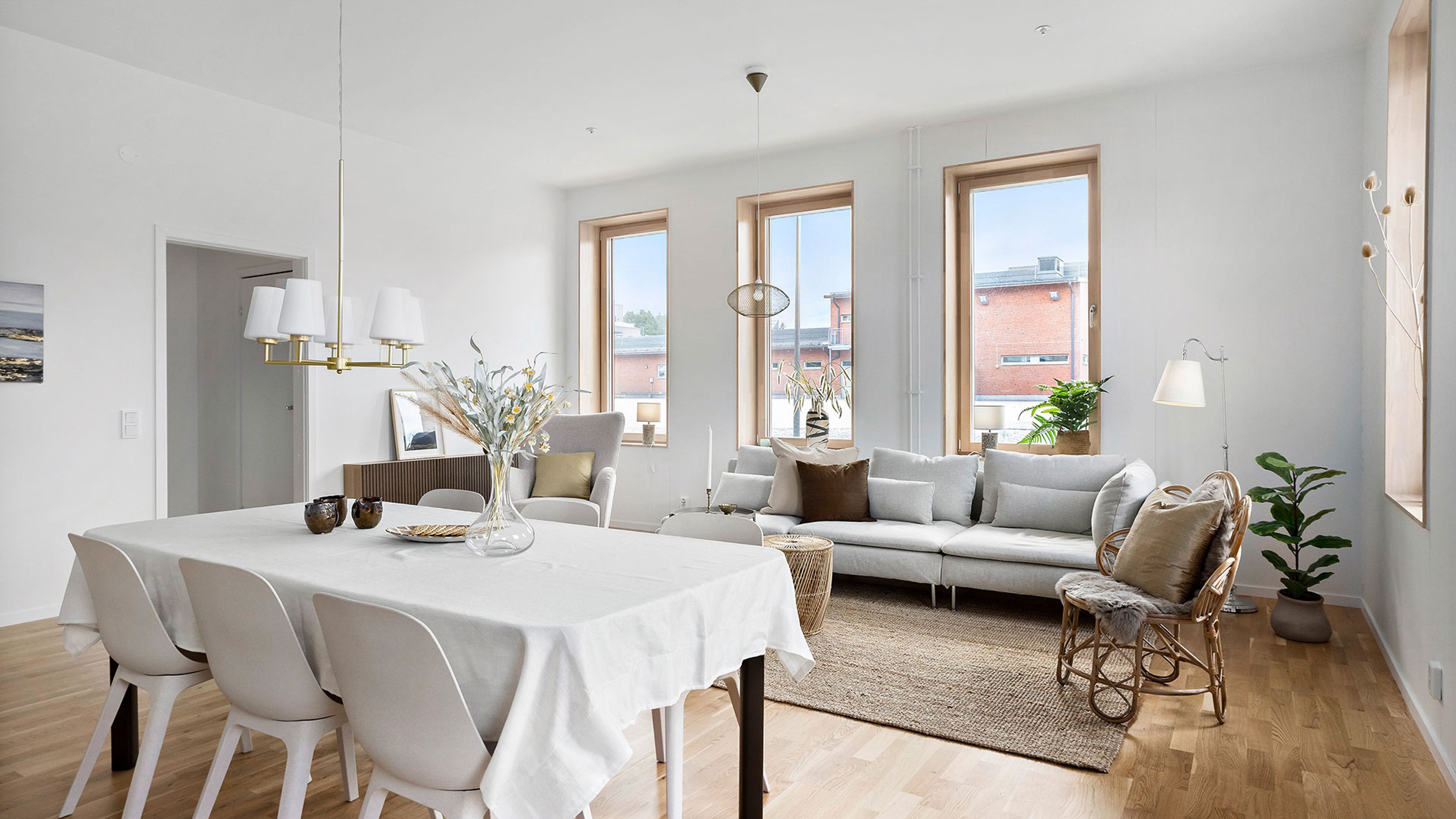 Foto på stort vardagsrum med många fönster, matbord i förgrunden och soffgrupp bakom