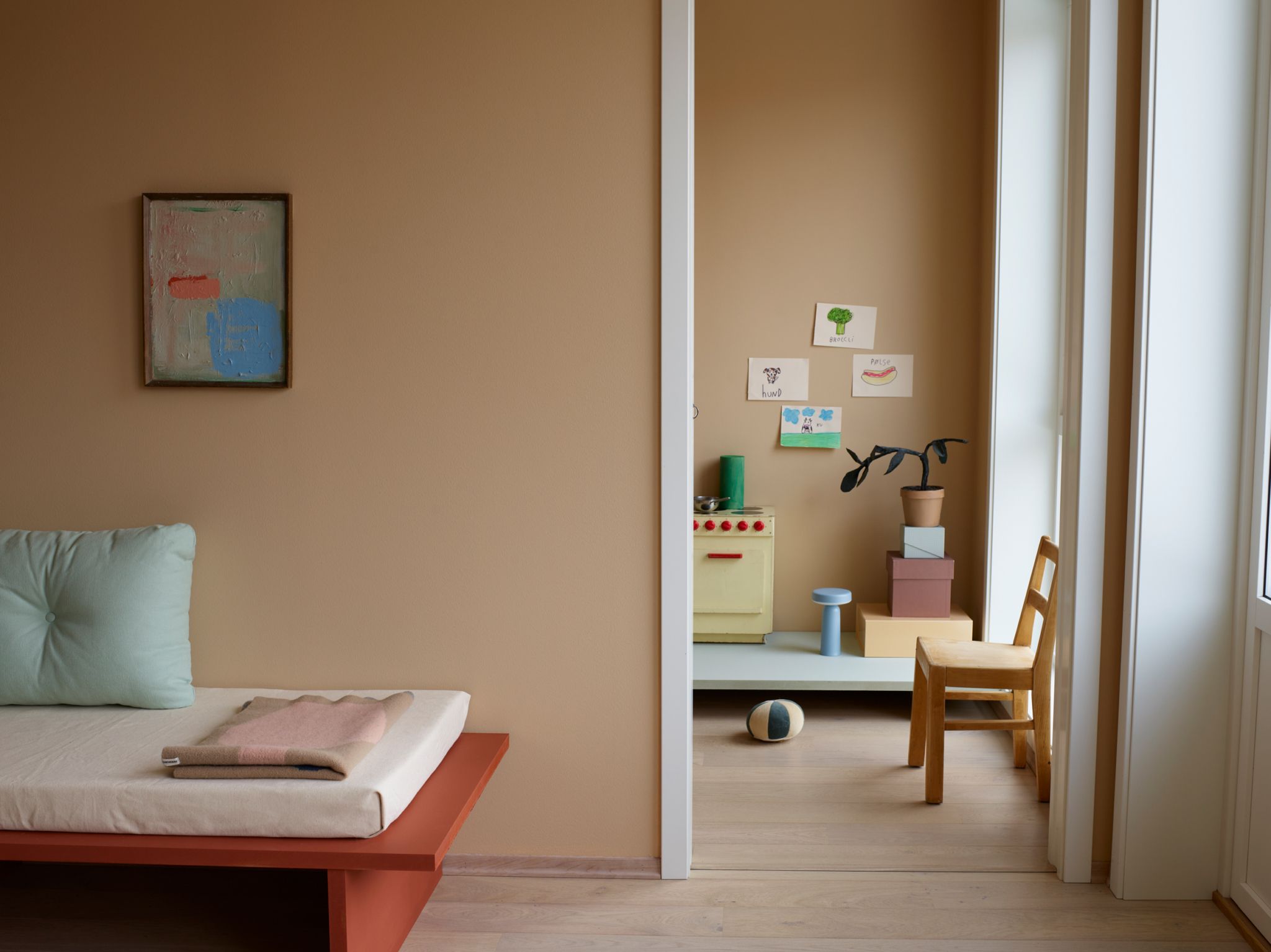 Ferskenfarget stue med selvsnekret sofa. Inngang til soverom med stol i tre og lekekomfyr til venstre i bildet.