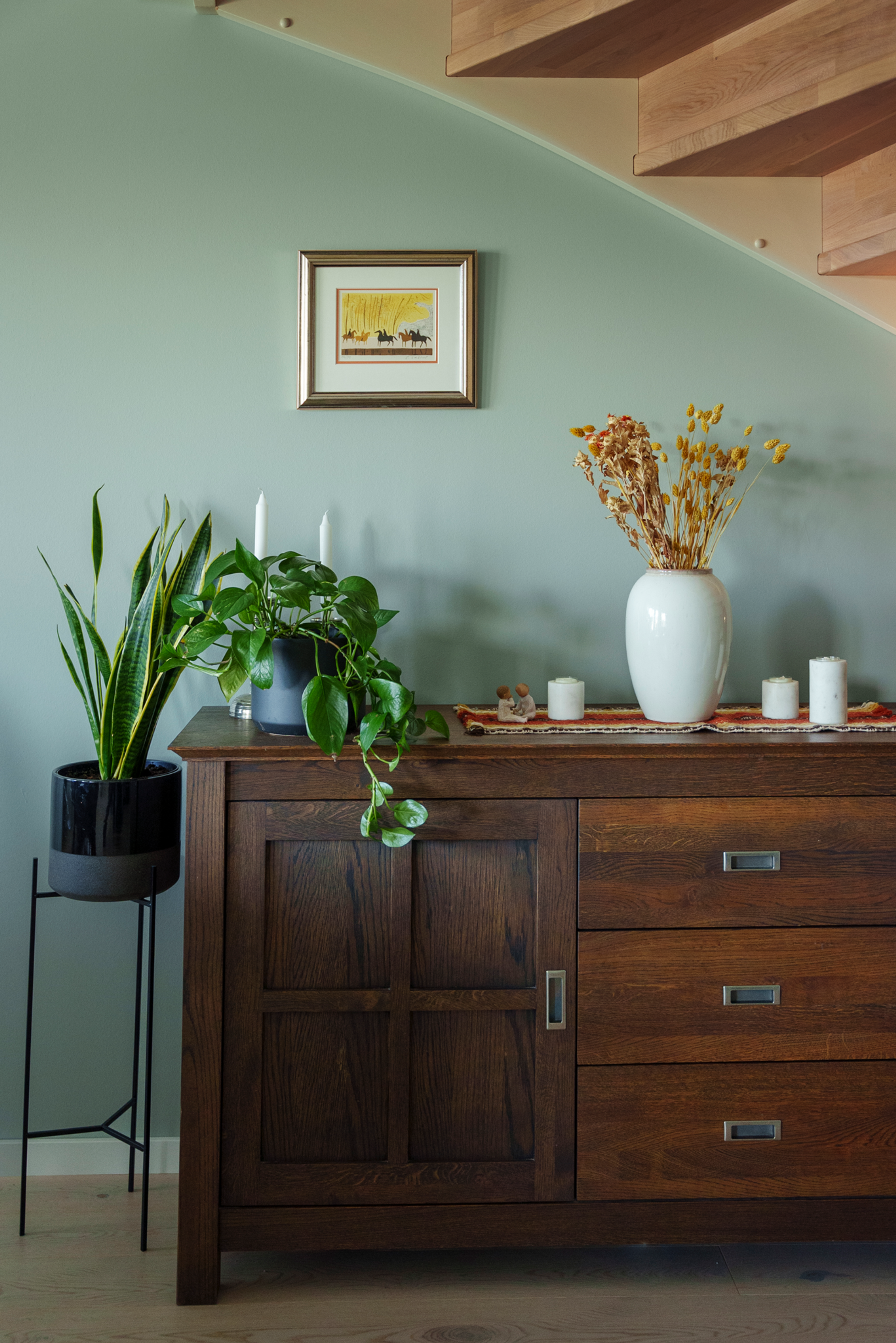 Detalj av en brun kommode mot en lysegrønn vegg med et lite bilde hengende over.