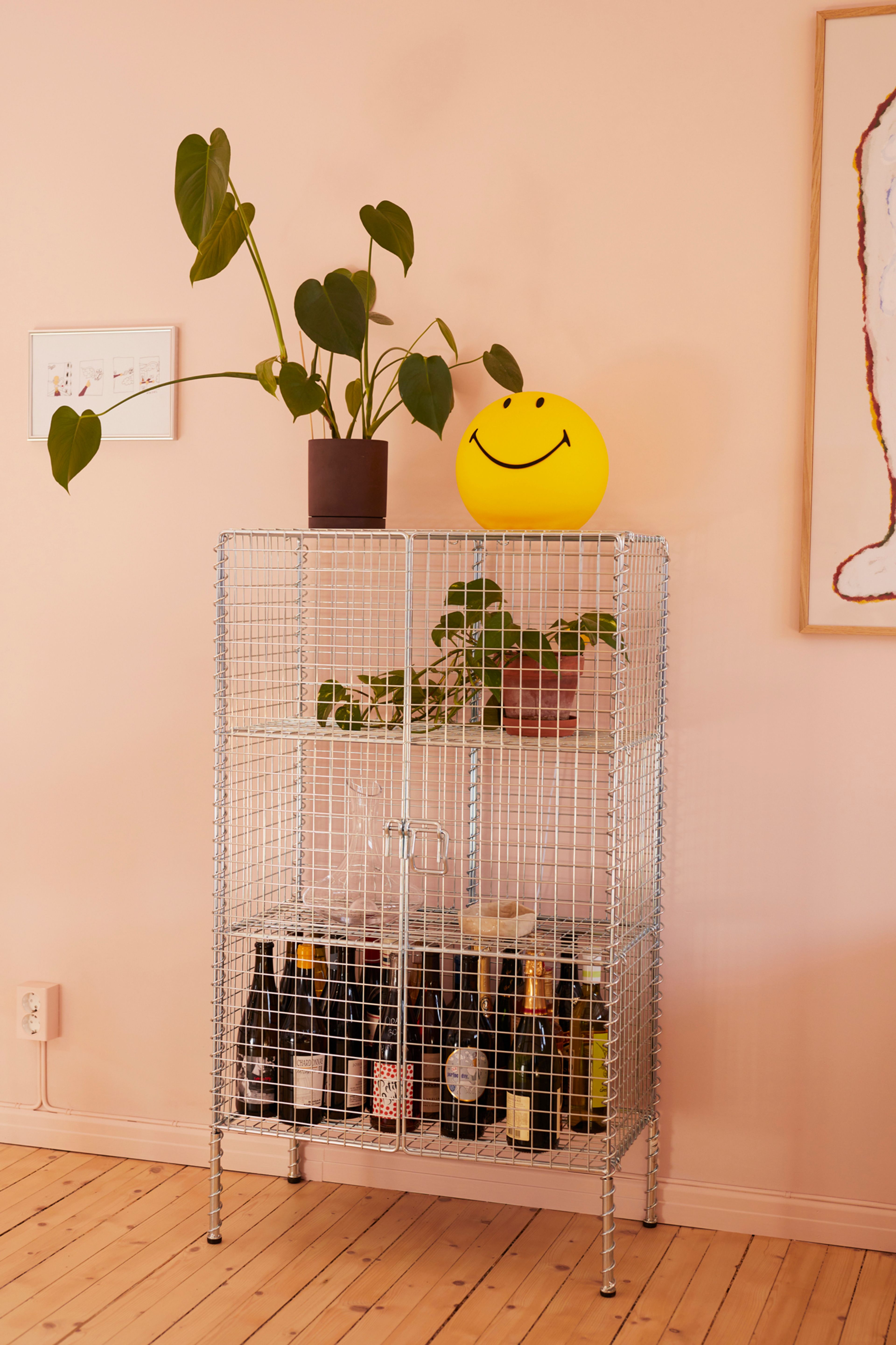 Skap i metall med en smiley-lampe og en plante oppå.