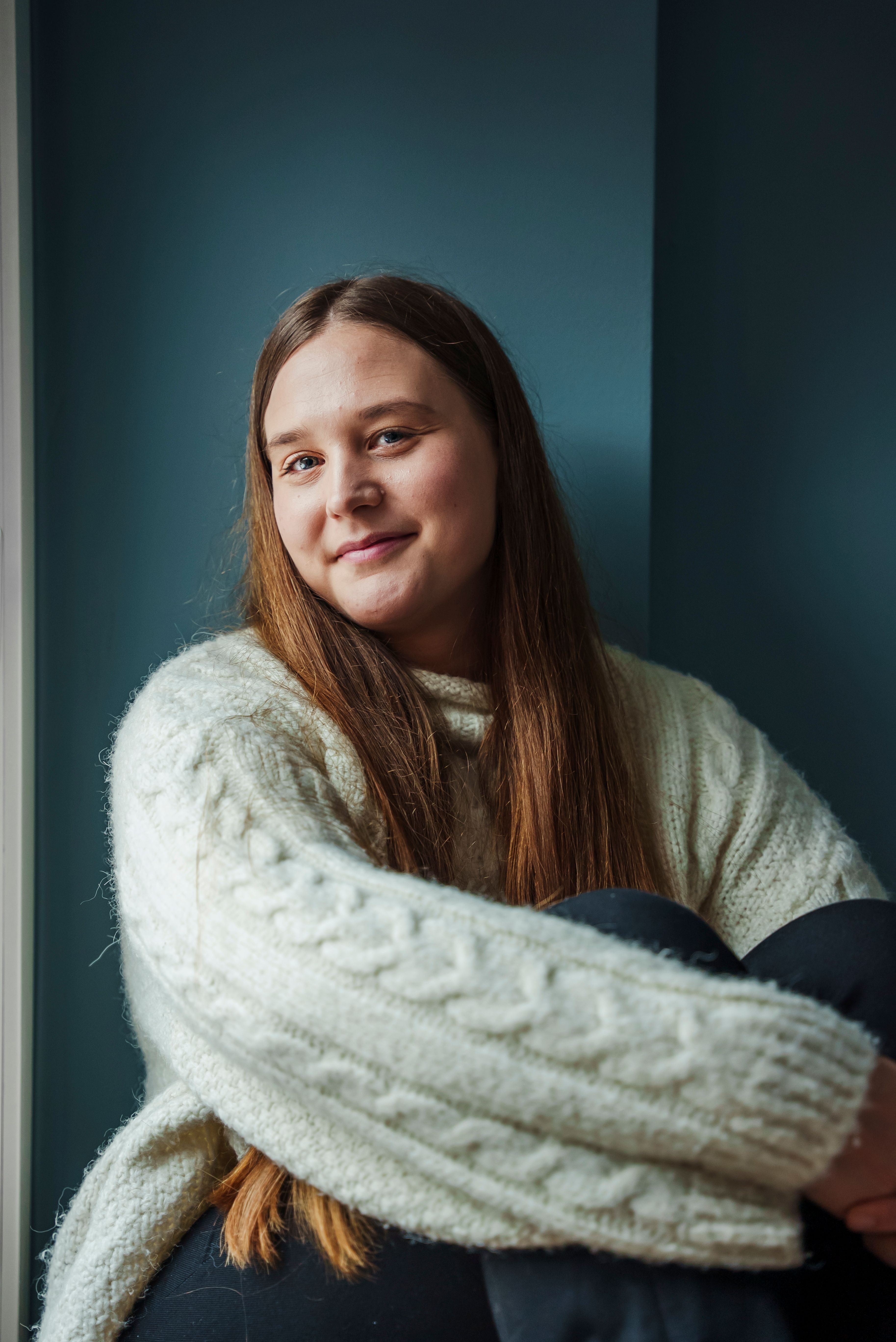 Kristine Istad sitter lent mot en mørk vegg og smiler mot kamera