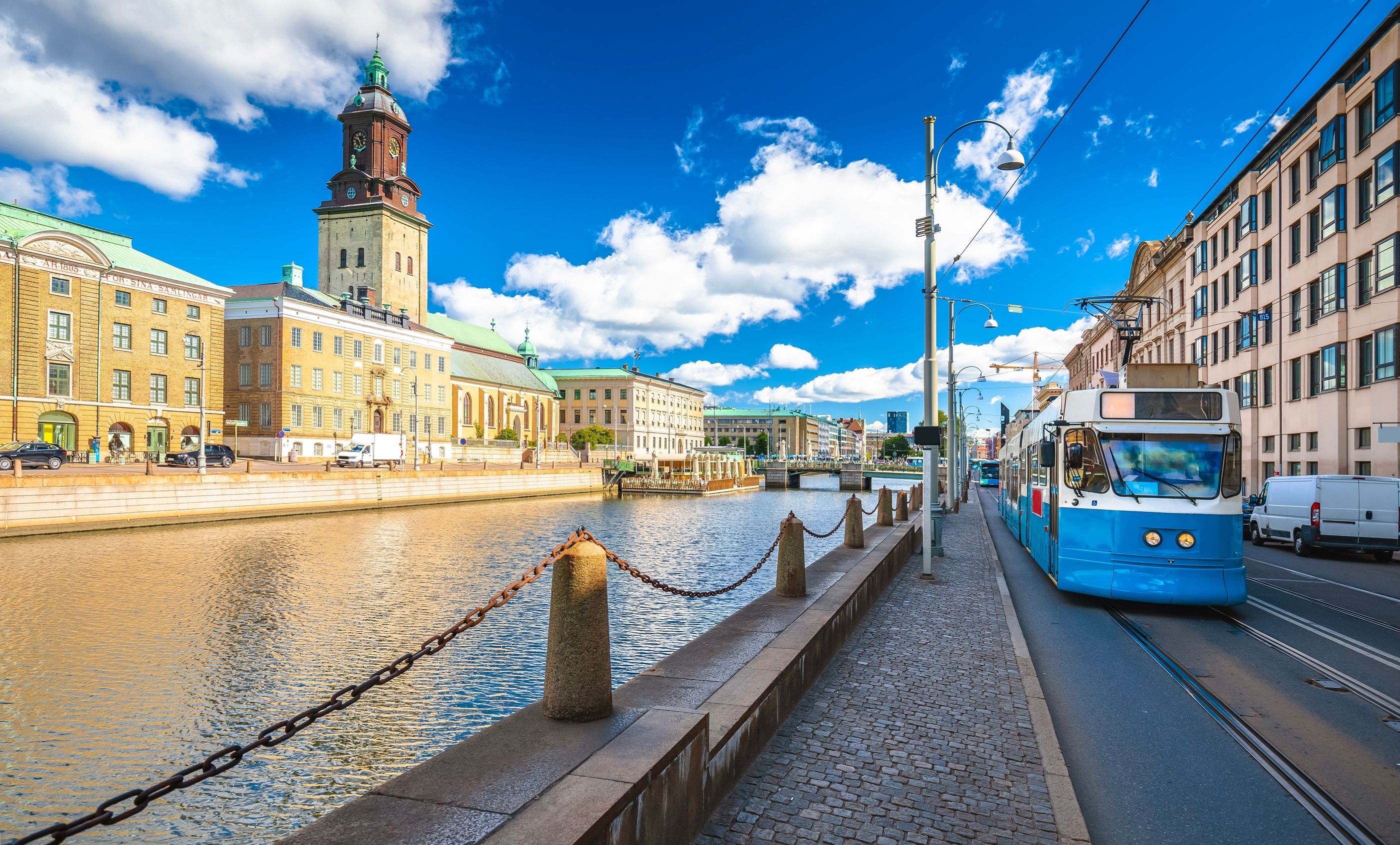 En blå trikk kjører ved elva i Gøteborg. Vakre bygninger ved siden av.