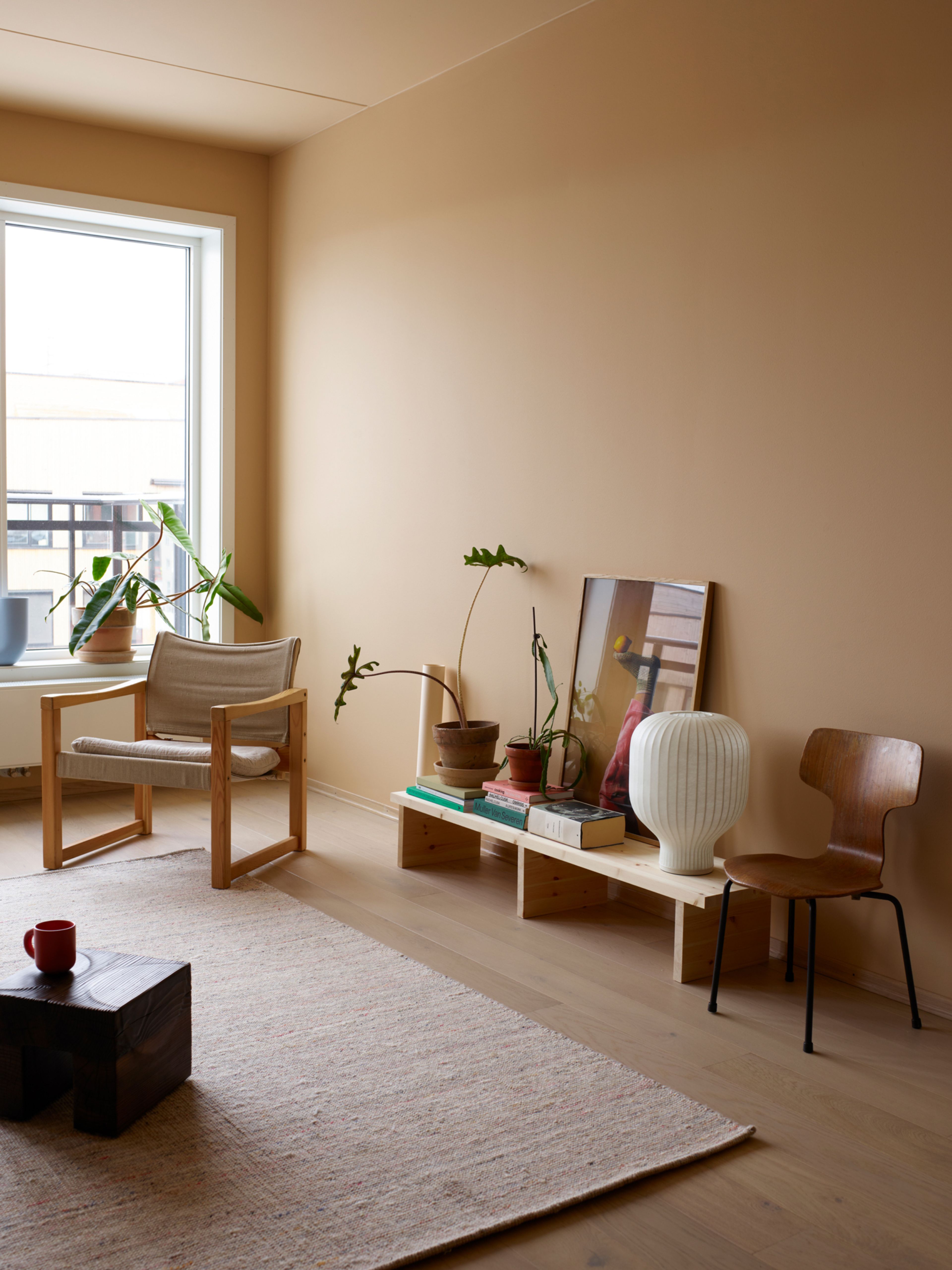 Ferskenfarget stue med lenestol i tre, beige gulvteppe og lav skjenk med pyntegjenstander.