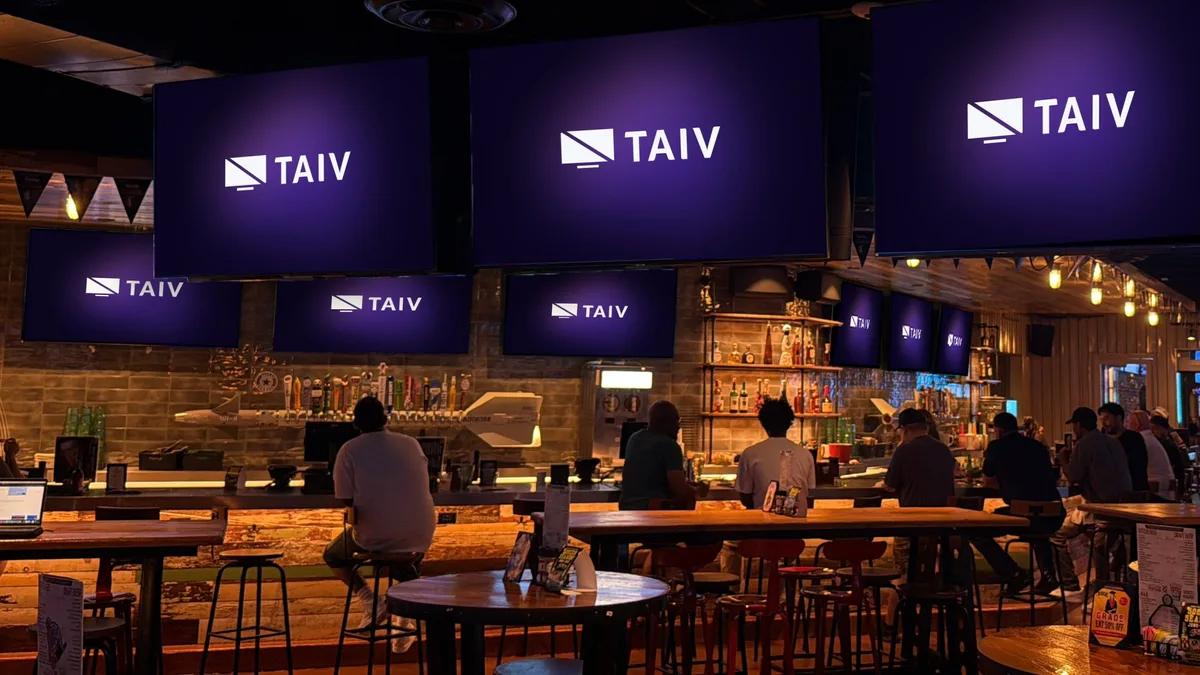 A wall of Taiv screens above a bar, with patrons watching out of home