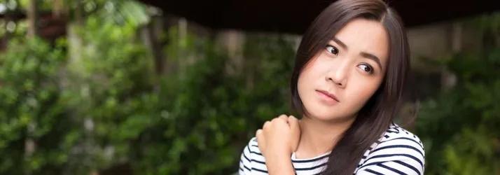 Woman in a striped top holding her shoulder outdoors