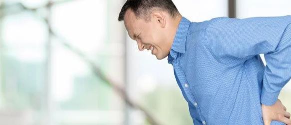 Man in a blue checked shirt wincing and holding his lower back