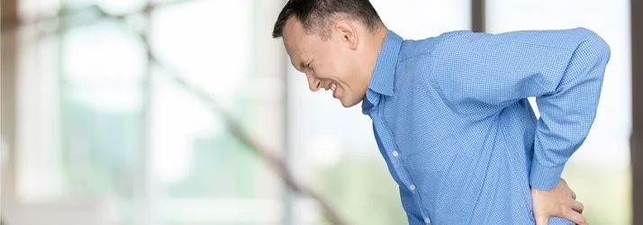Man in a blue checked shirt wincing and holding his lower back