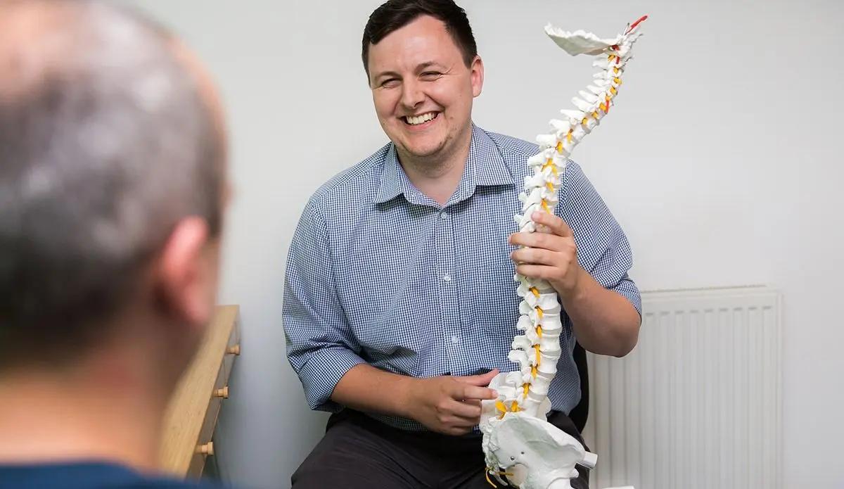 A chiropractor explaining scoliosis to a patient using a spine model