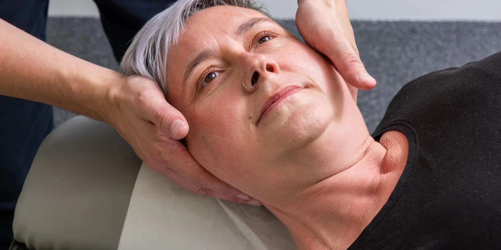 A practitioner’s hands cradling the head and neck of a woman lying face up on a treatment couch