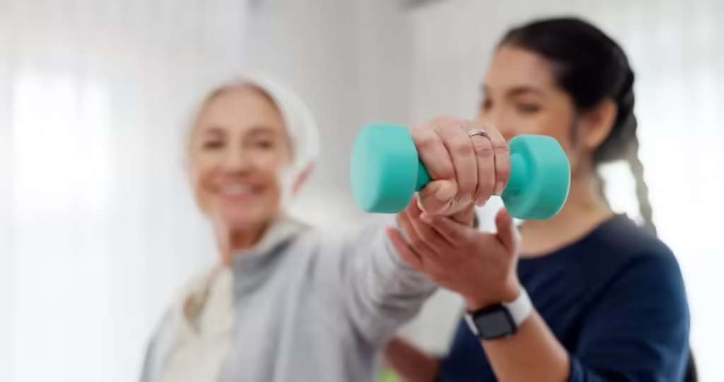 A practitioner supporting the arm of an older woman as she lifts a small hand weight during a rehabilitation exercise