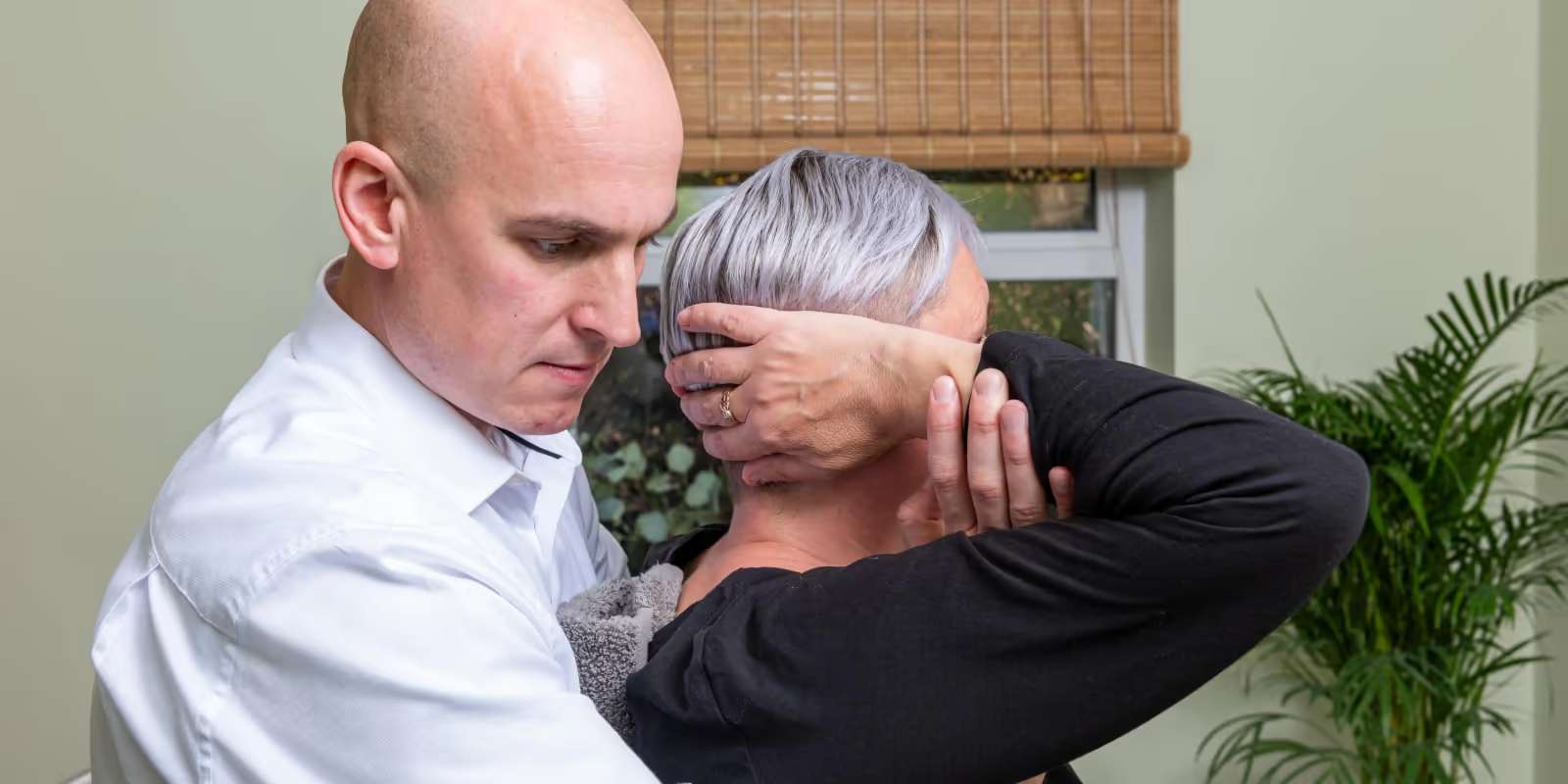 A chiropractor in a white shirt supporting a patient’s head and neck with both hands during treatment