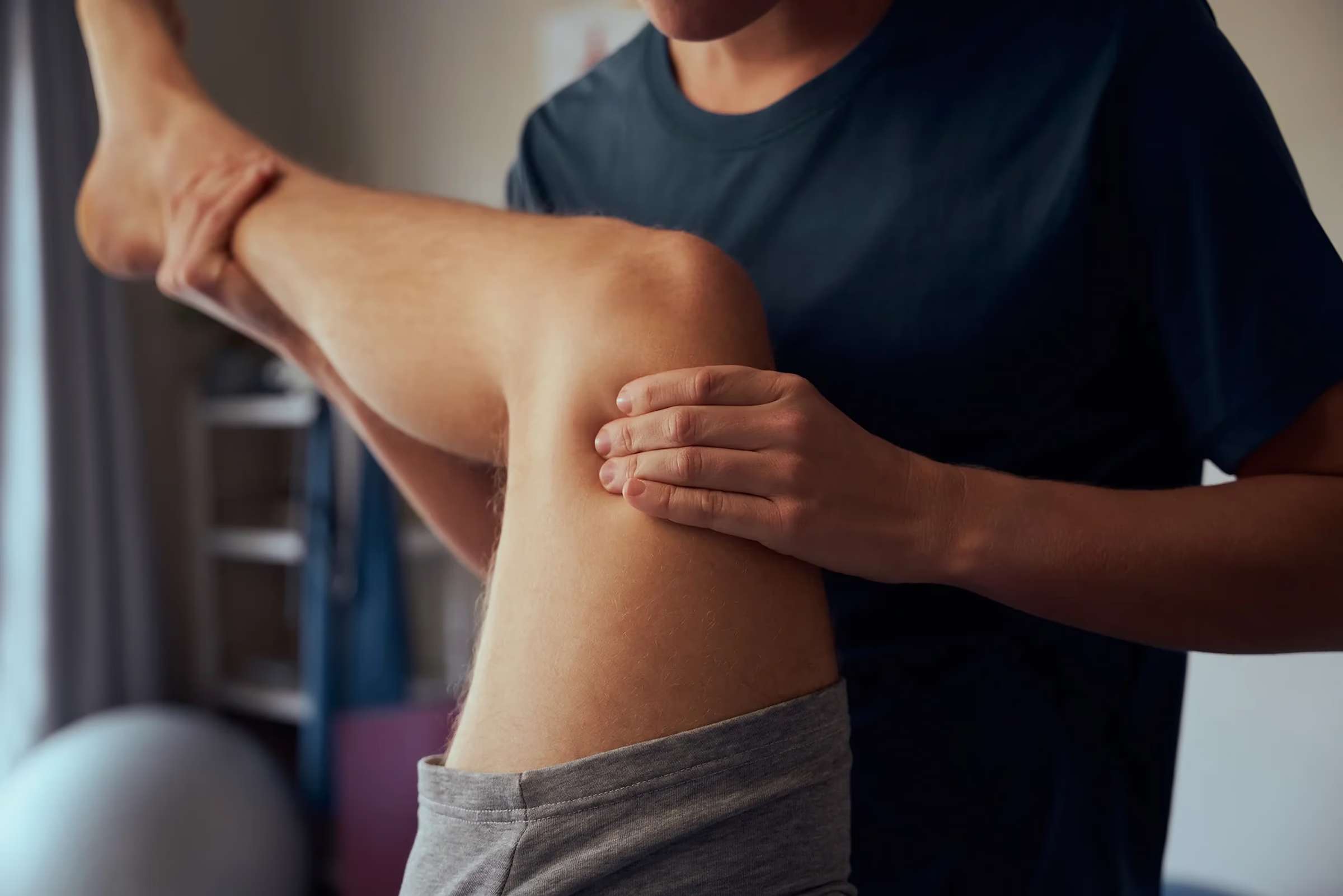 A practitioner supporting a patient’s raised leg and pressing on the back of the thigh during treatment