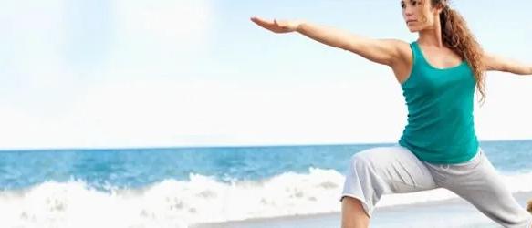 Woman in a lunging yoga pose with arms outstretched on a beach