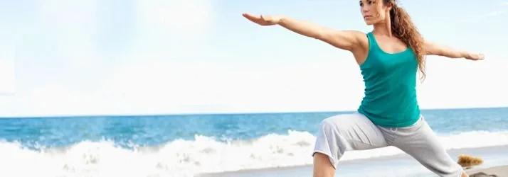 Woman in a lunging yoga pose with arms outstretched on a beach