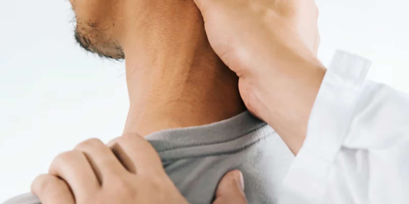 A practitioner’s hand pressing on the side of a man’s neck, with the other hand resting on his shoulder