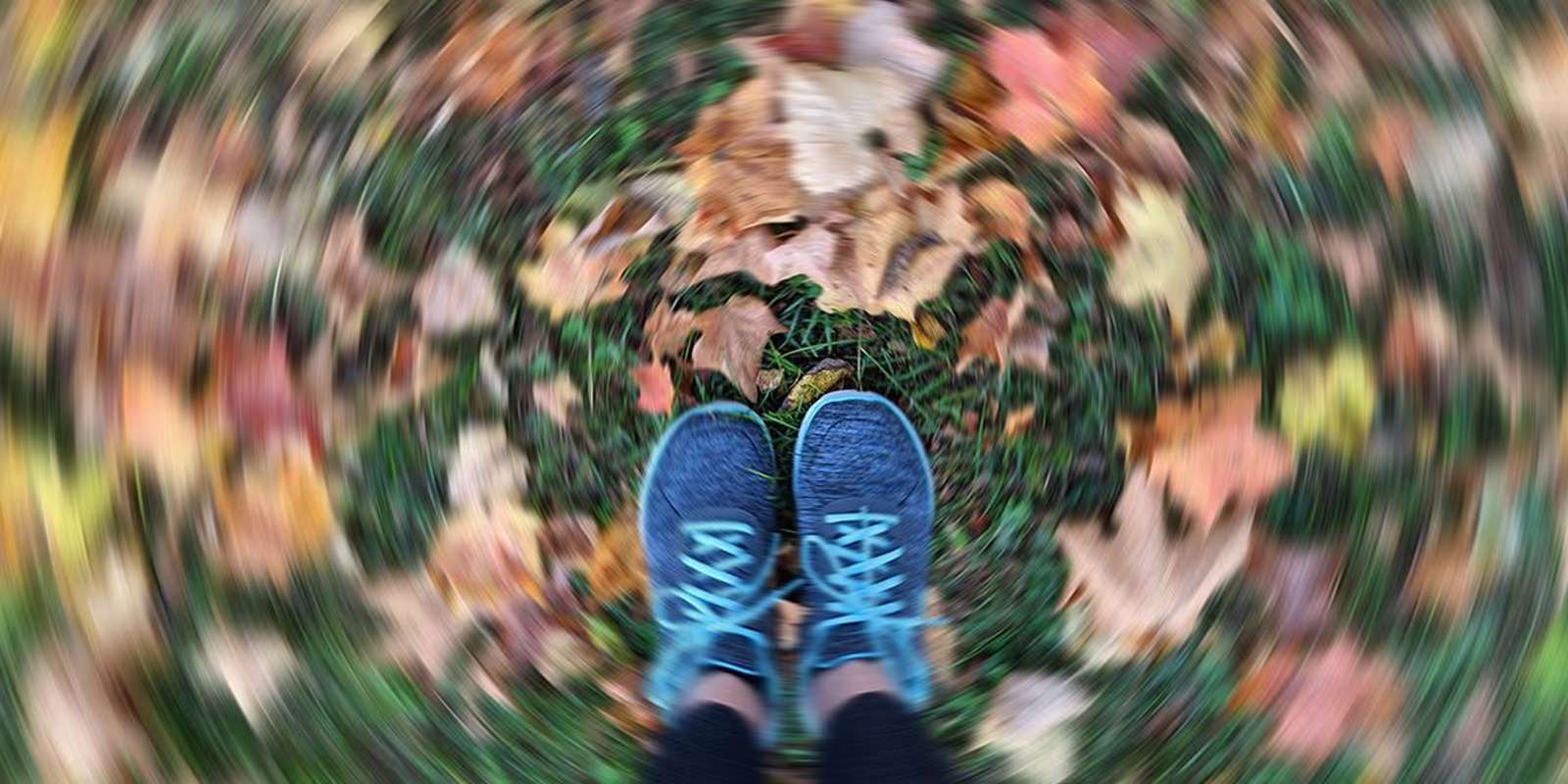 Looking down at a pair of blue trainers on autumn leaves, blurred as if spinning