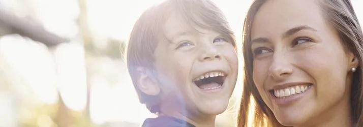 Laughing boy next to a smiling woman outdoors in sunlight
