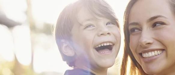 Laughing boy next to a smiling woman outdoors in sunlight