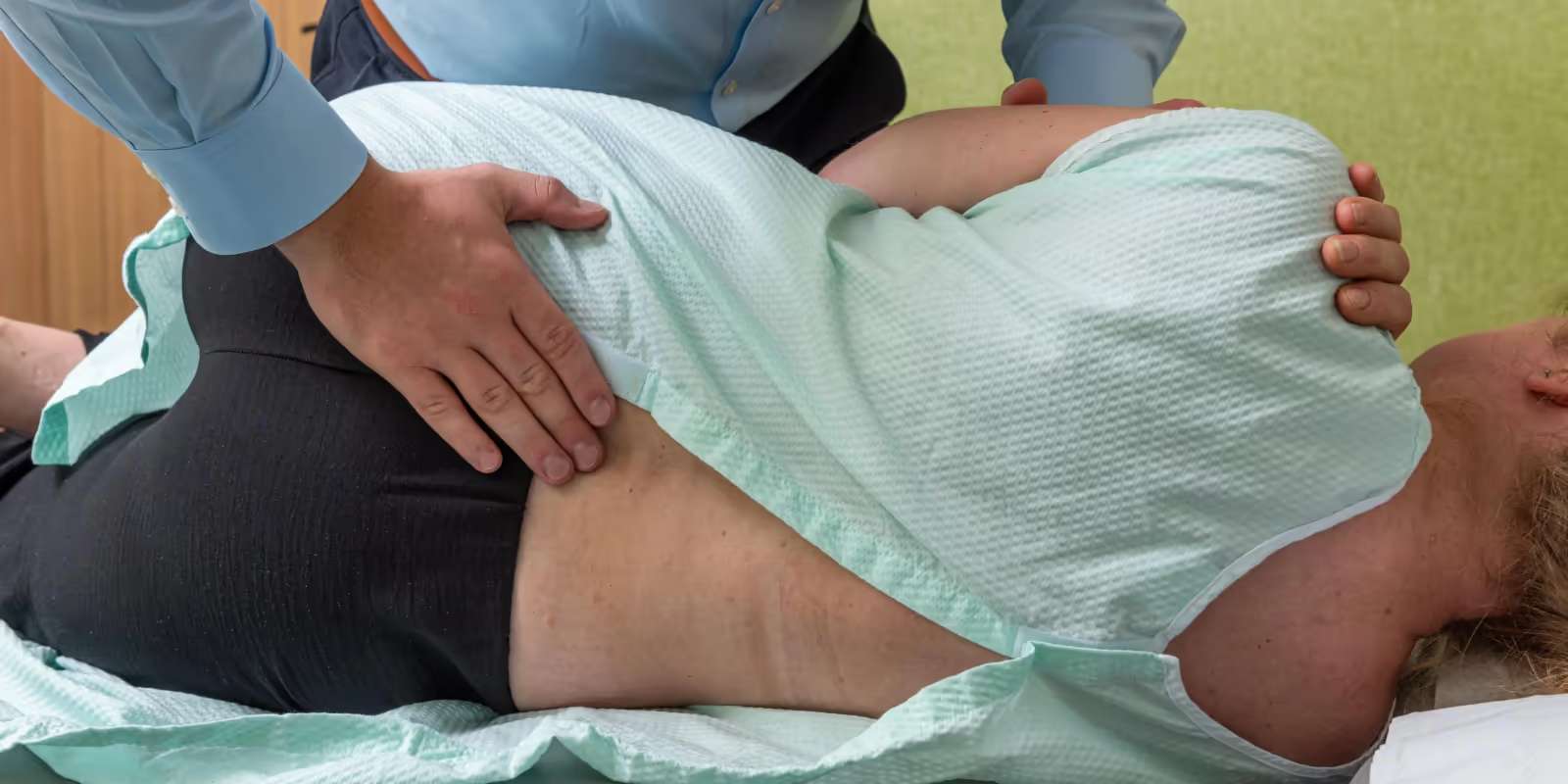 A practitioner’s hands on the lower back and shoulder of a patient lying on their side in a treatment gown