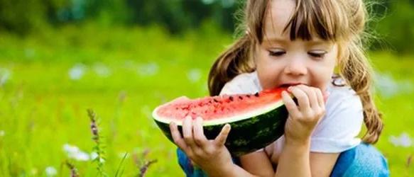 Young girl eating a slice of watermelon on grass