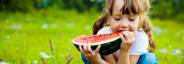 Young girl eating a slice of watermelon on grass