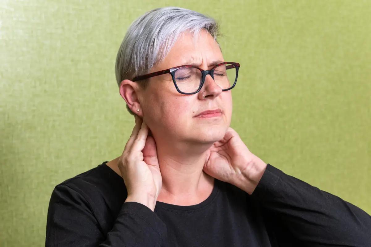 A woman holding the back of her neck in discomfort