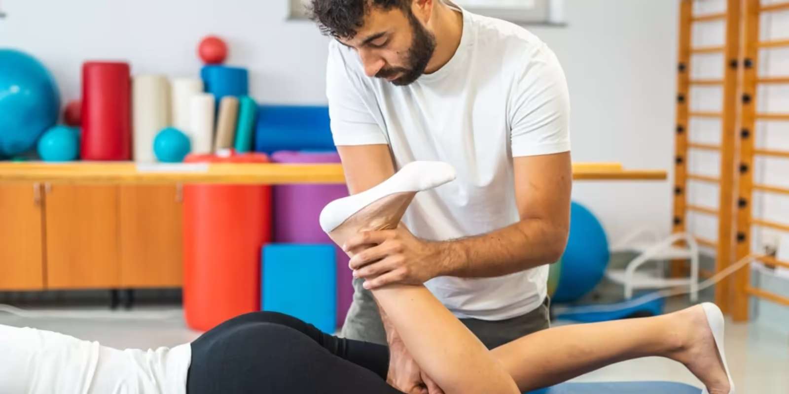 A practitioner bending the knee of a patient lying on a mat in an exercise studio