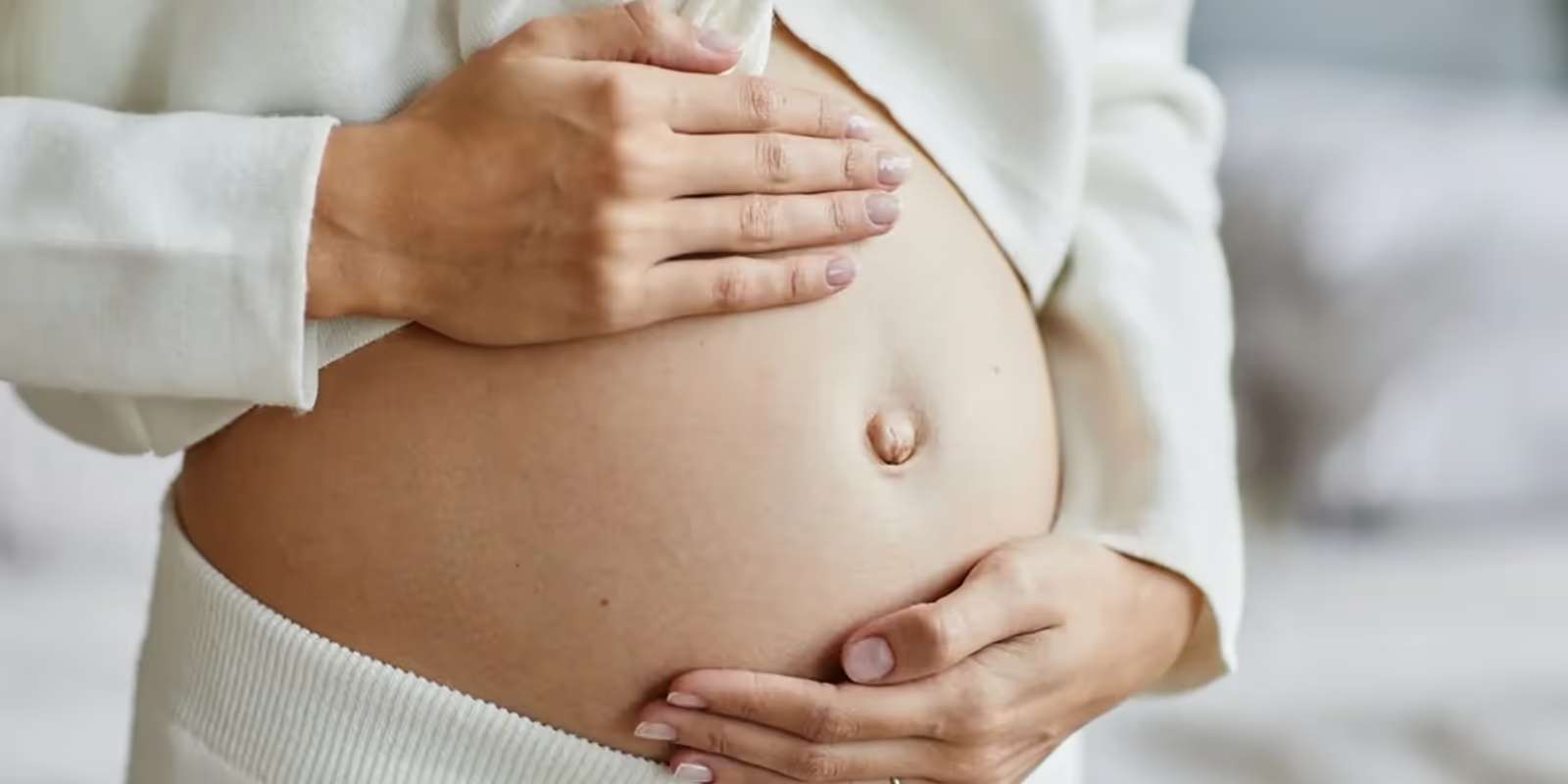 A pregnant woman holding her bare bump with both hands