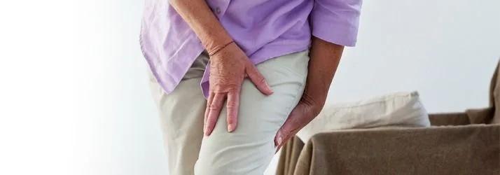 Older woman in a lilac top holding the back of her thigh