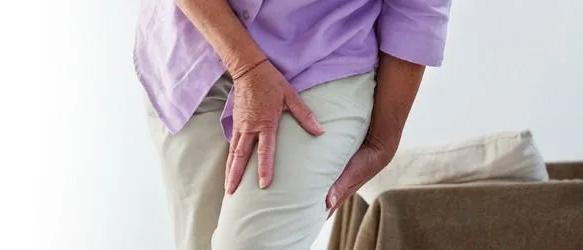 Older woman in a lilac top holding the back of her thigh