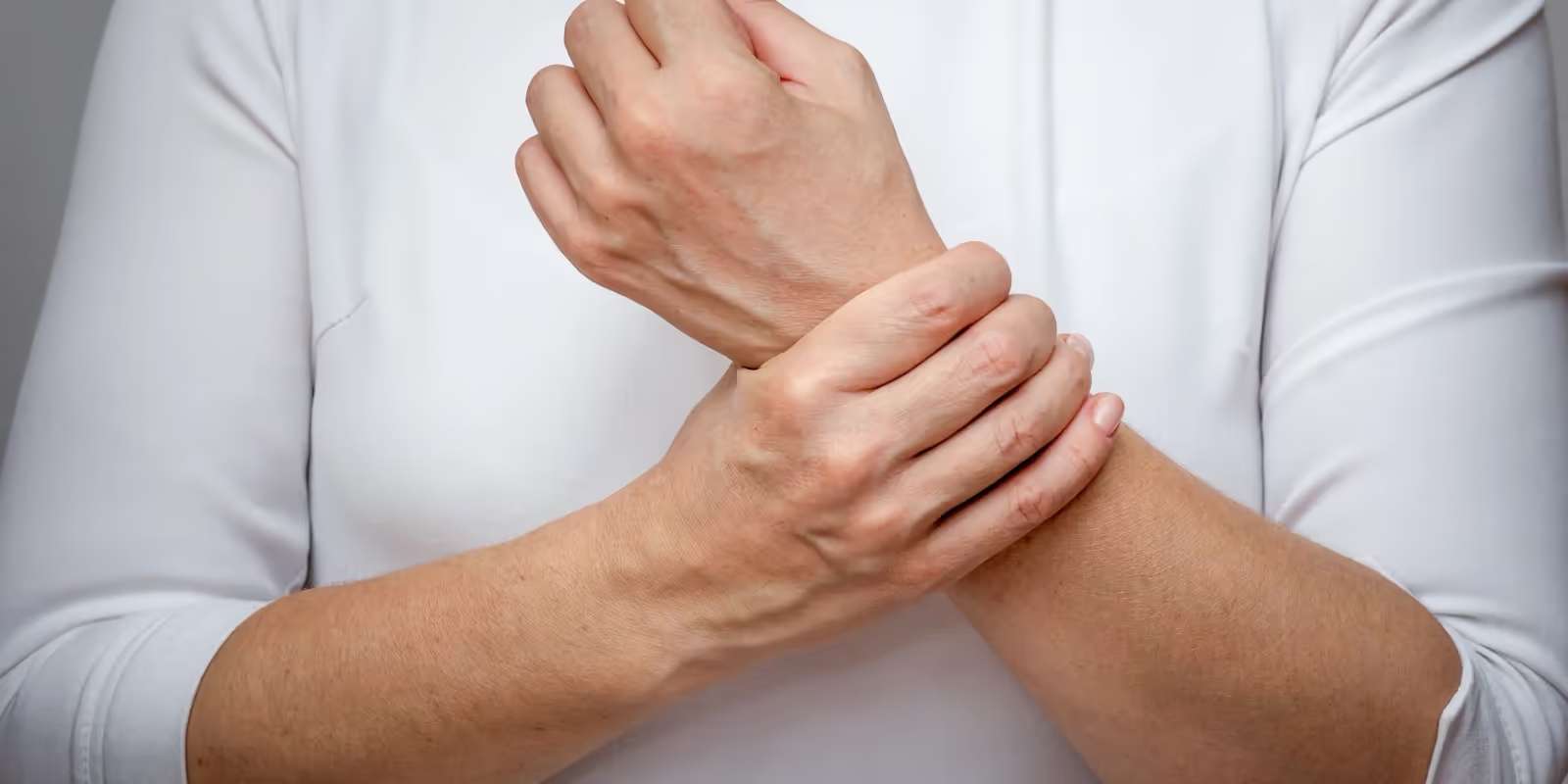 A person in a white top holding one wrist with the other hand