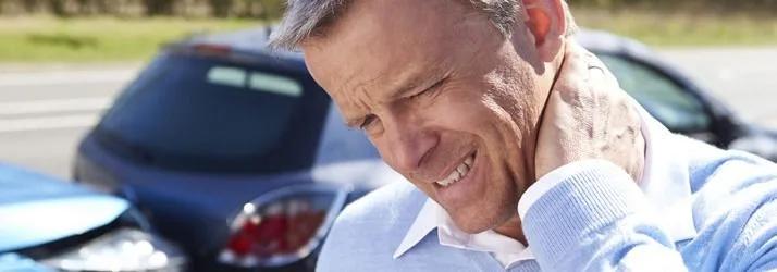 Man wincing and holding his neck in front of a crashed car