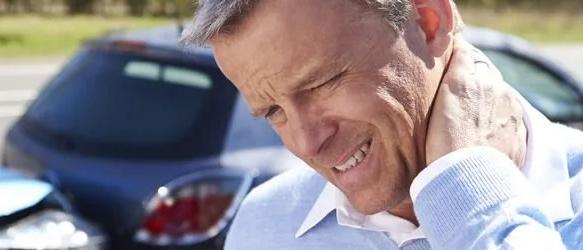 Man wincing and holding his neck in front of a crashed car