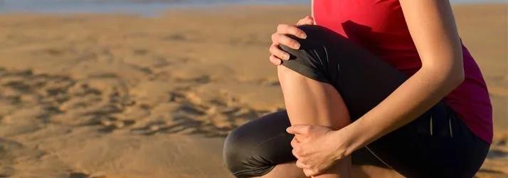 Runner in a red top crouching on a beach, holding her knee