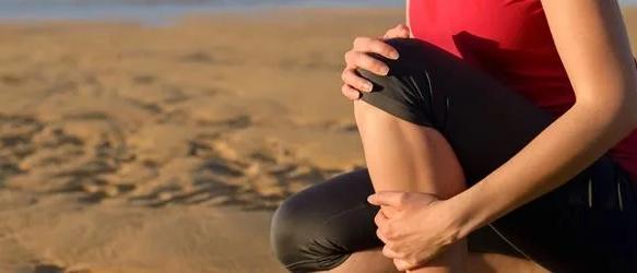 Runner in a red top crouching on a beach, holding her knee