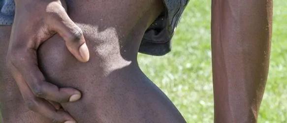 Close-up of a person gripping their thigh above the knee on a grass field