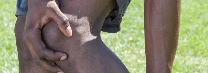 Close-up of a person gripping their thigh above the knee on a grass field