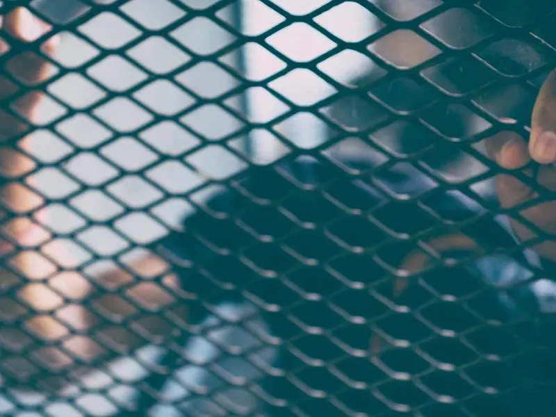 A person's hand reaching through a chain link fence