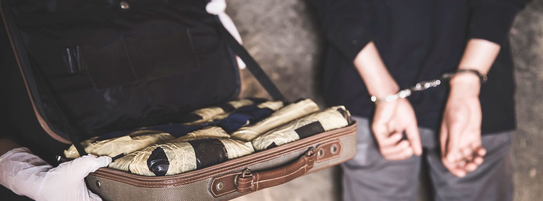 Person in handcuffs next to a briefcase full of drugs