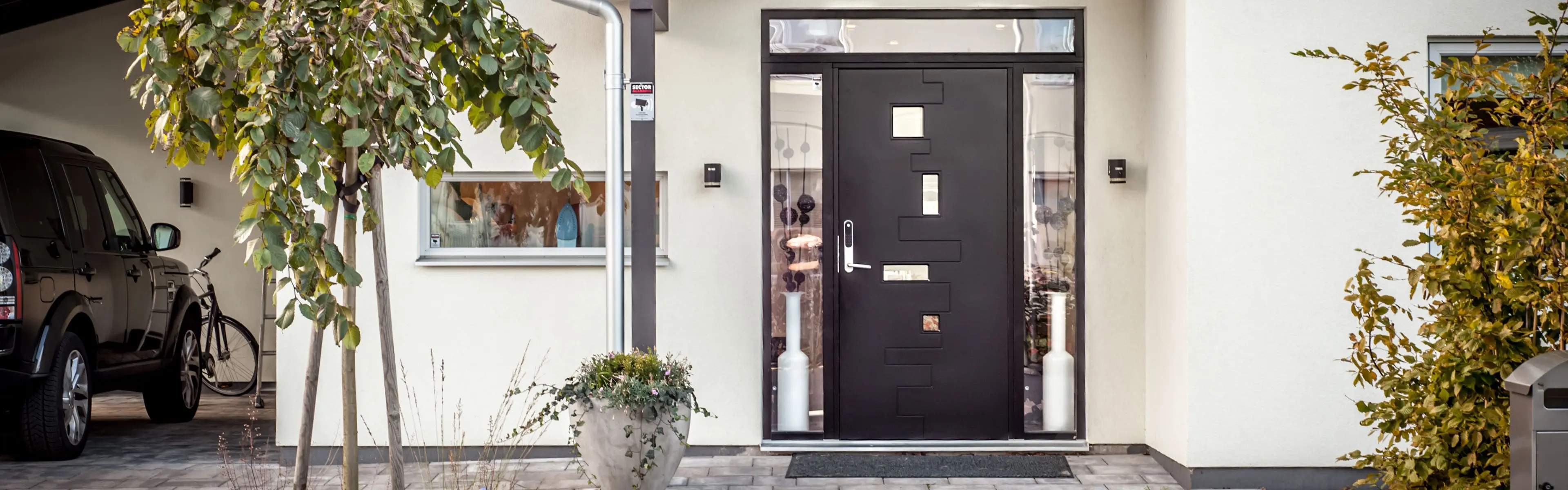 Hvitt murhus med sort inngangsdør og sidefelt i glass