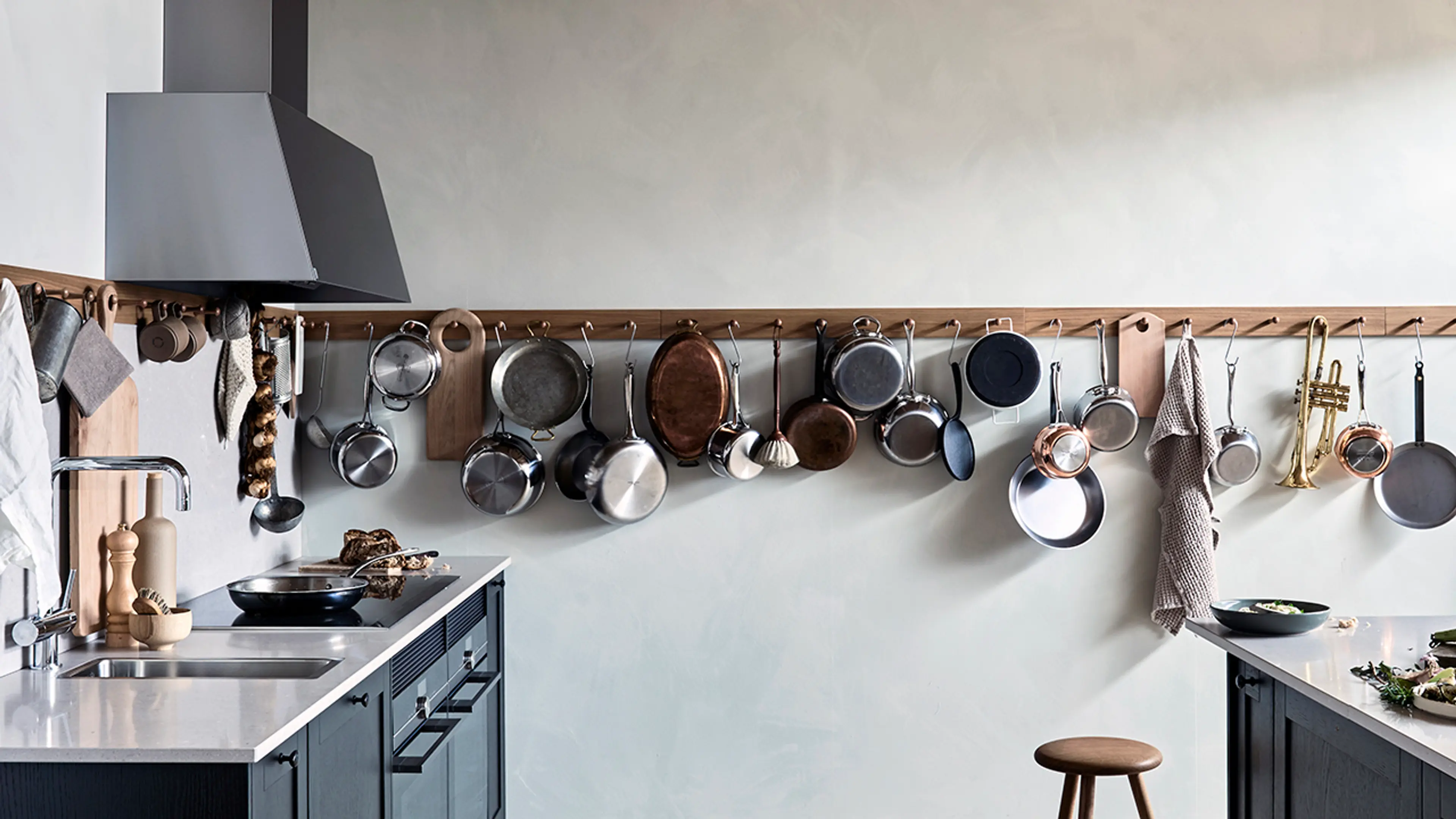 Svart kjøkkenvifte som matcher kjøkkenet i et landlig kjøkken med lang knaggrekke til kjøkkenredskaper.