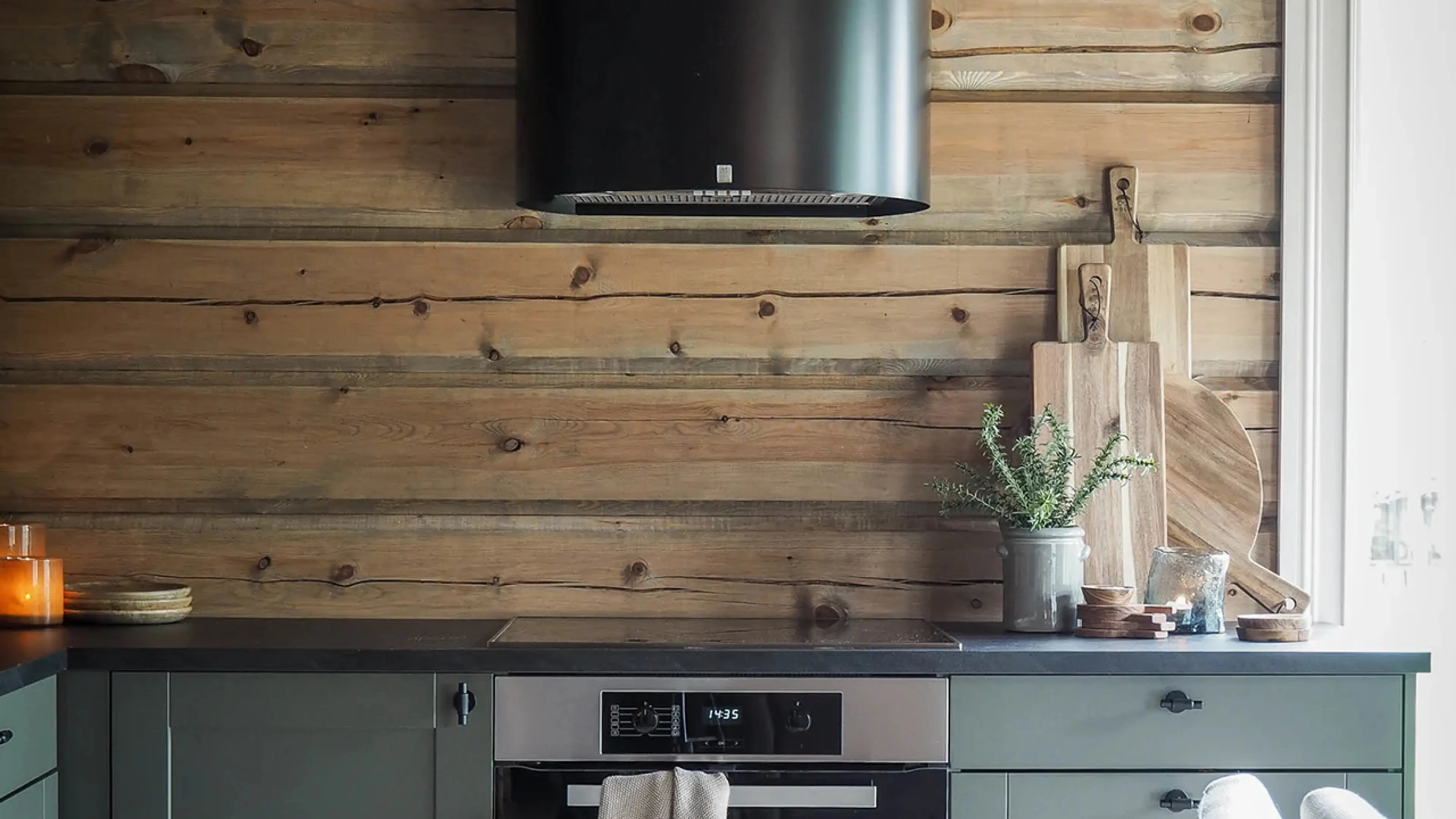 Tømmerhytte med hyttekjøkken i mørk grønnfarge, svart benkeplate og svart kjøkkenhette.