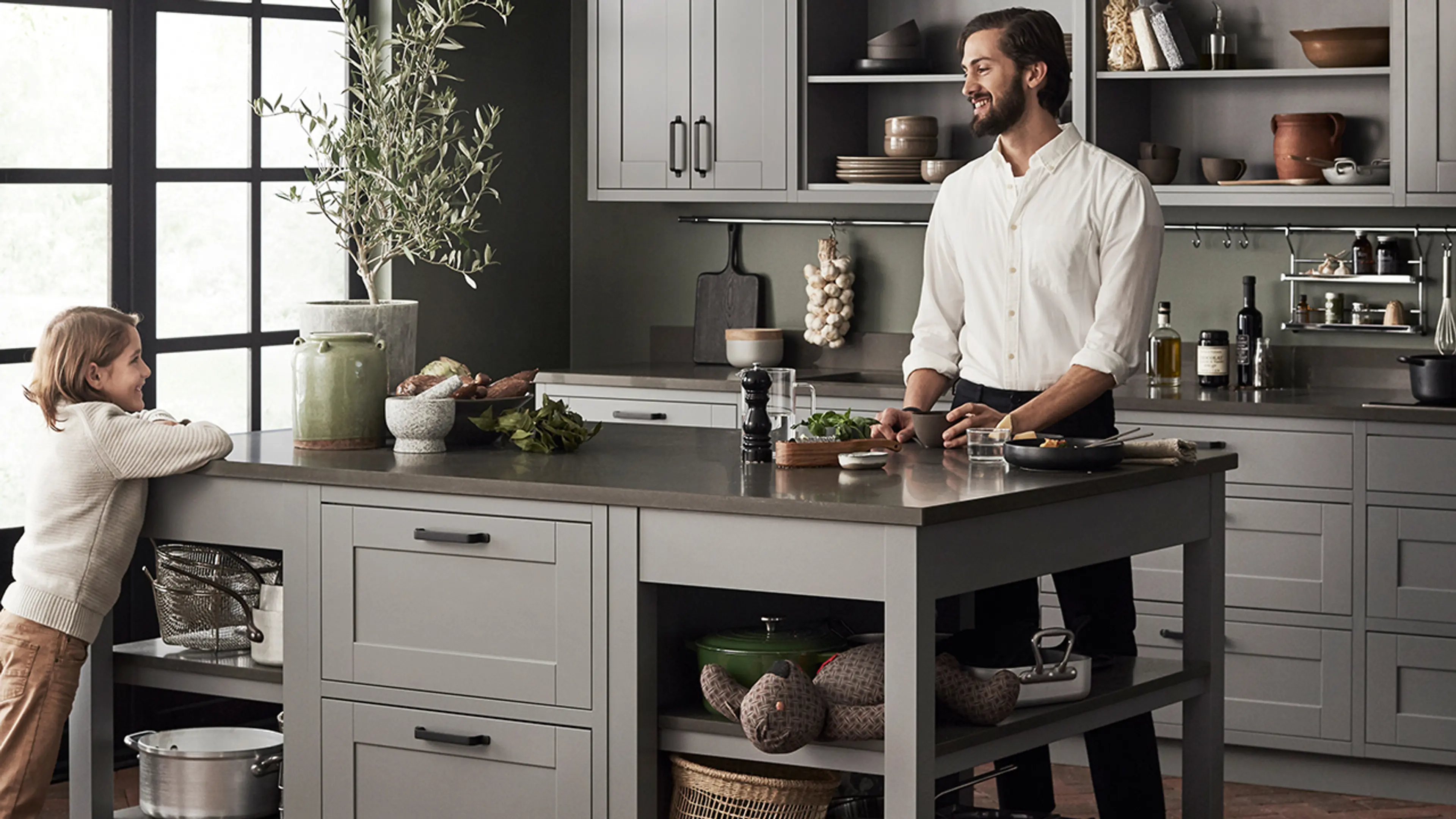 Far og sønn på et landlig kjøkken med kjøkkenøy med åpne hyller i hver ende.