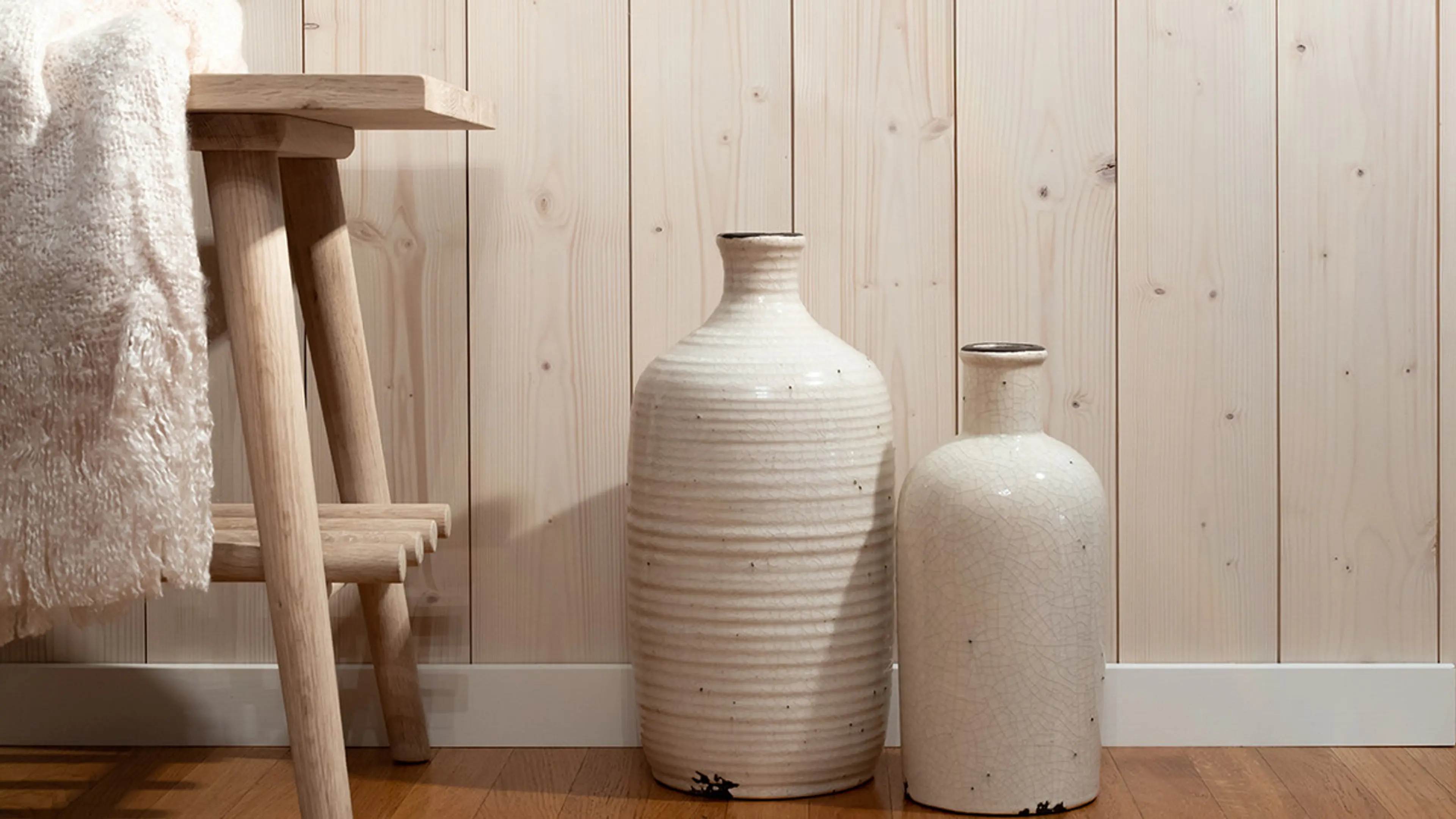 nærbilde av trepanel på vegg, med en krakk og keramikkpotter stående foran