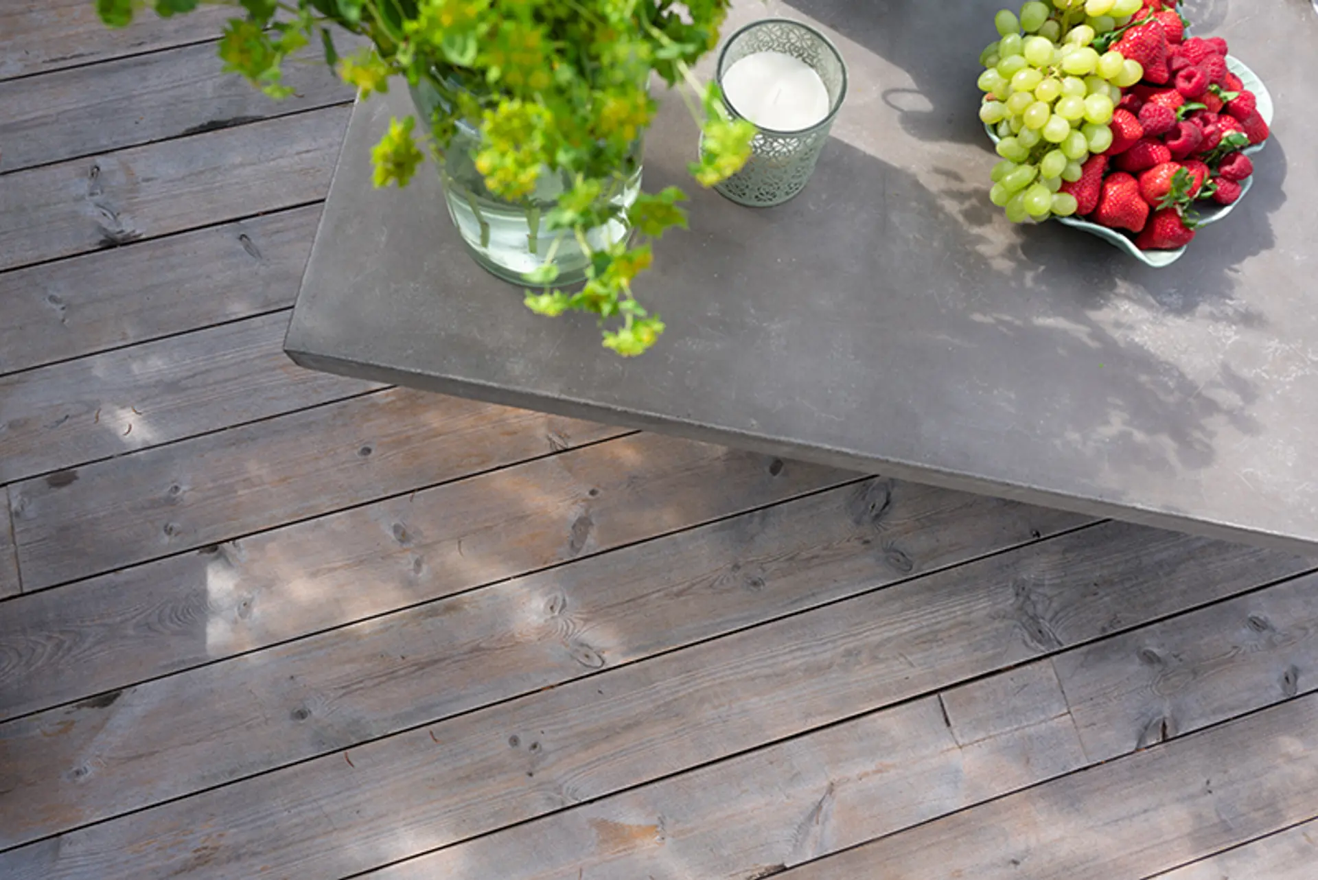 fruktfat og en vase med grønne plater står på et betongbord på en terrasse