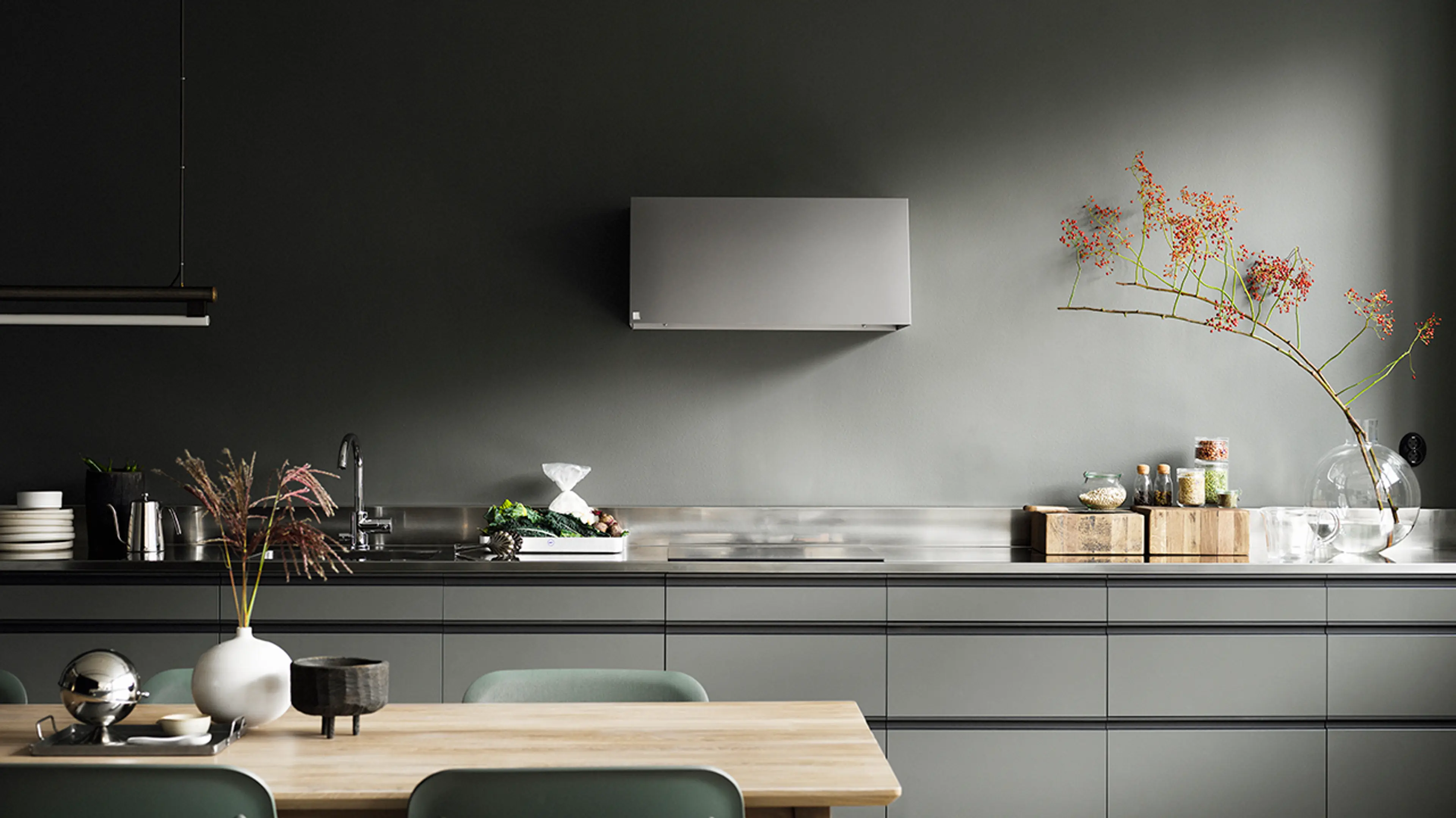 Grønt kjøkken med kjøkkenvifte og benkeplate i stål.