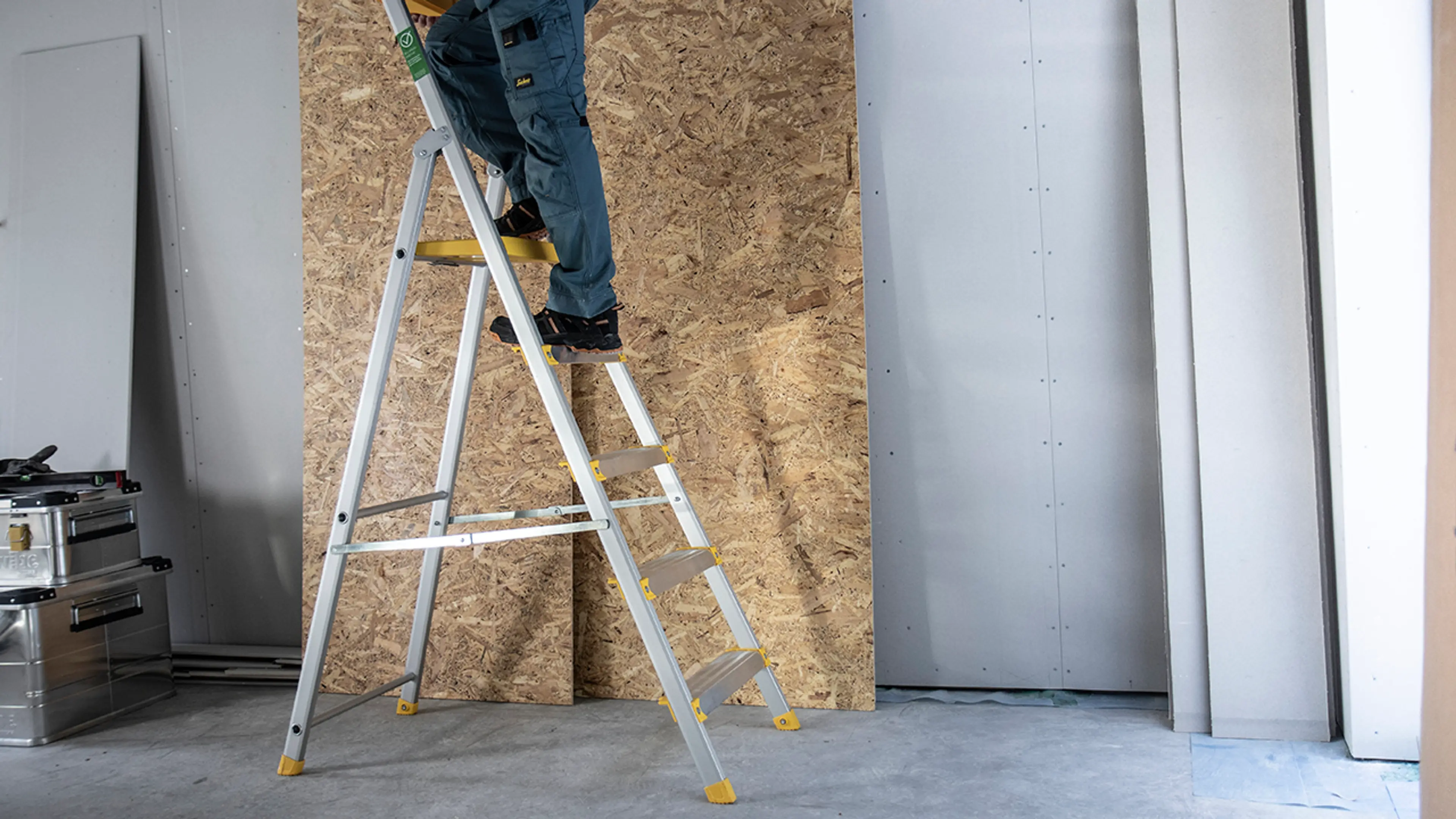 Mann som står på gardintrapp for å komme bedre tl i høyden på byggeplass.