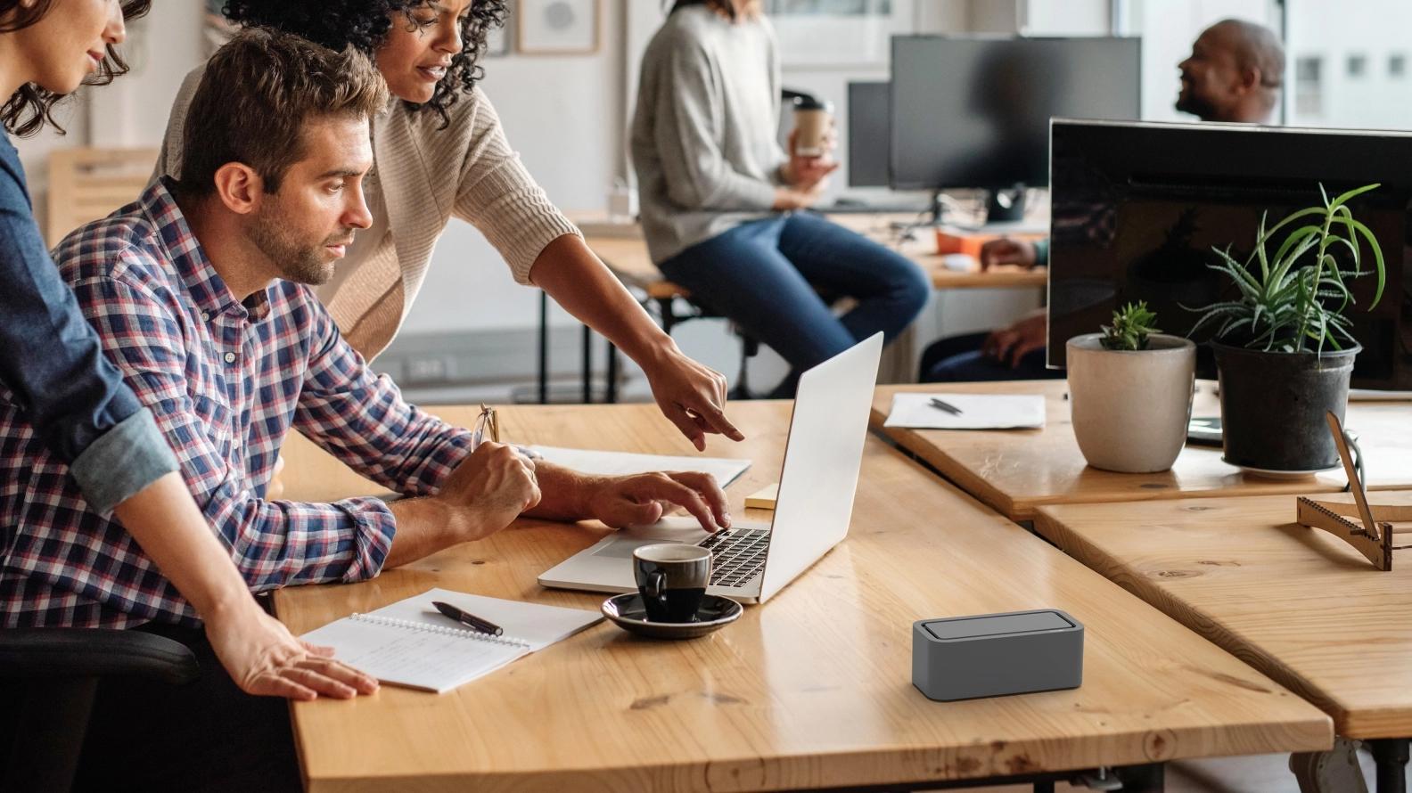 Multiple co workers pointing at a laptop while discussing and taking notes.