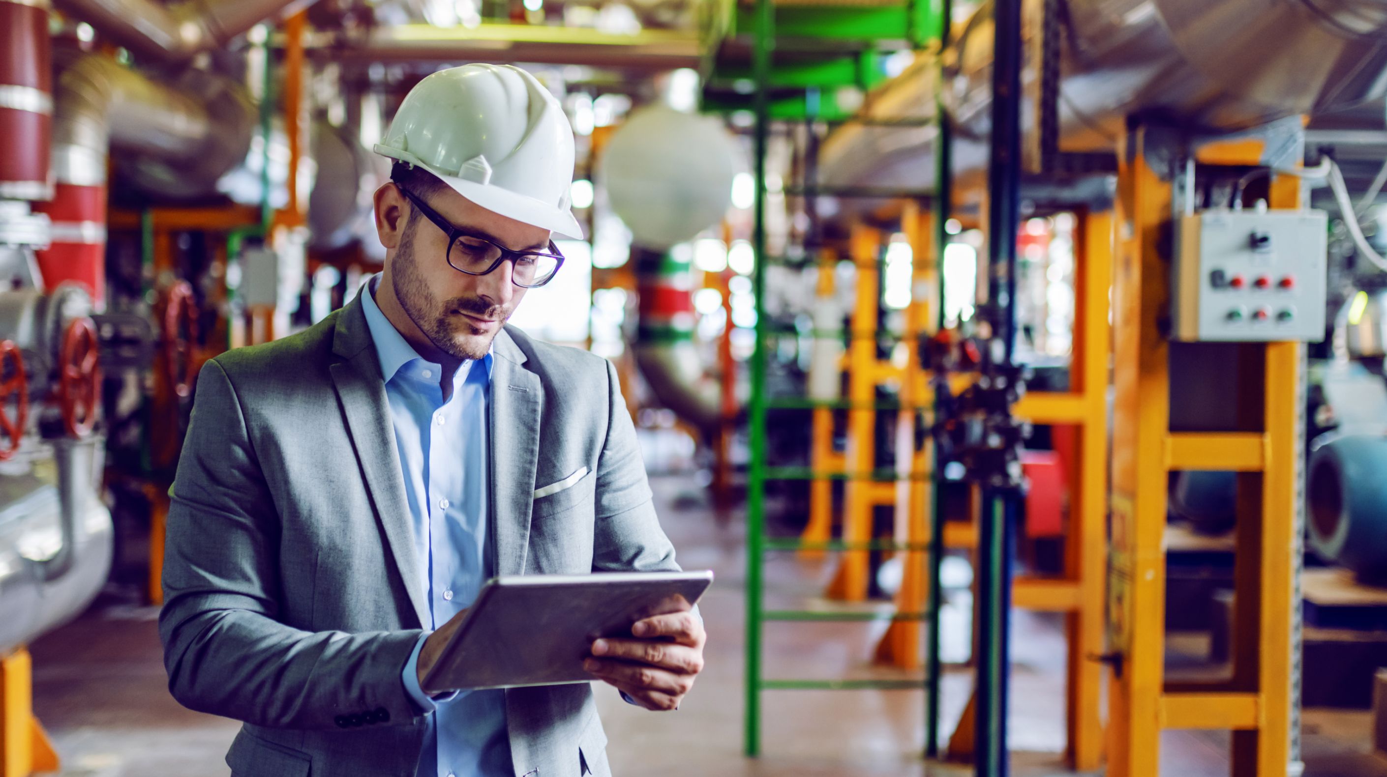 Factory worker looking down at a tablet to check on the industrial devices behind them.