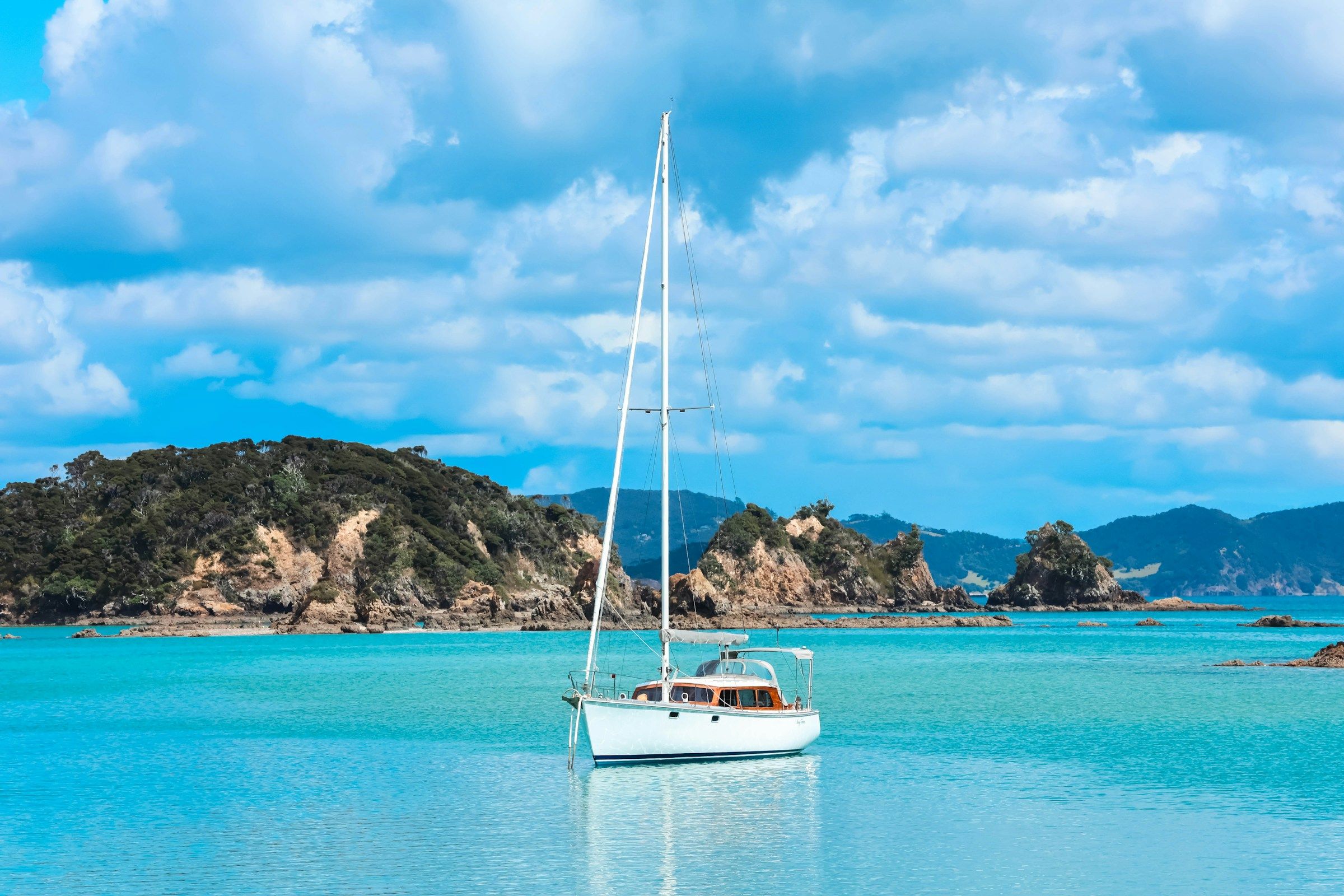 A white sailboat on turquoise water near rocky islands